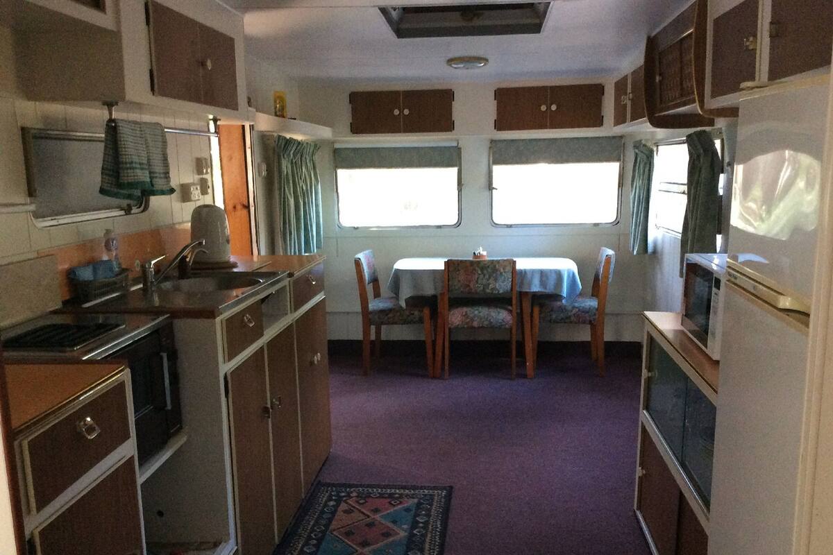 Une cuisine compacte pour camping-car, équipée d’un évier, d’une cuisinière et d’un coin repas avec des chaises et une table.