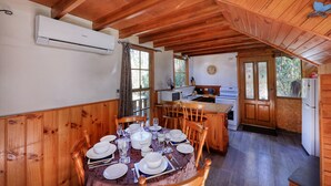 Une cabane en bois comprenant un coin repas aménagé, une cuisine équipée d’appareils électroménagers de base et de grandes fenêtres offrant une vue sur l’extérieur.