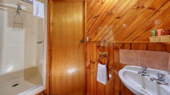 Une salle de bain aux murs lambrissés, équipée d’une baignoire, d’un lavabo et d’une douche.