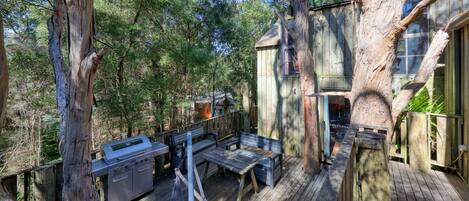 A wooden deck with a grill, benches, and a hammock.
