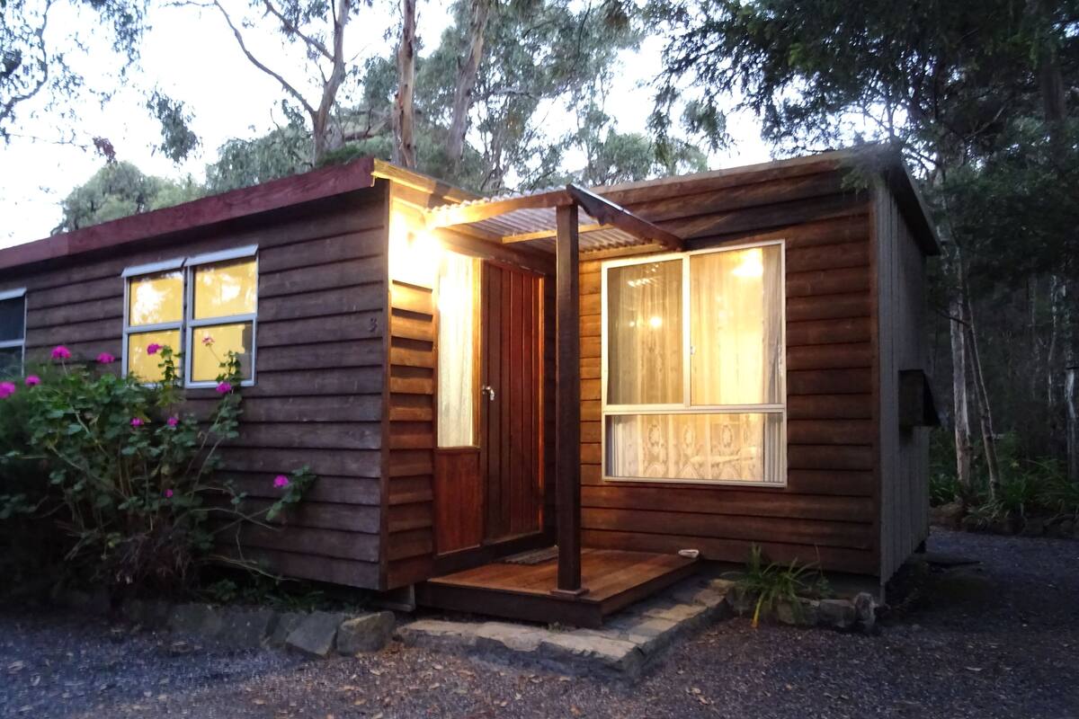 Une petite cabane en bois avec une véranda, une fenêtre avec des rideaux et une porte.