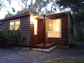 A small wooden cabin with a porch, a window with curtains, and a door.