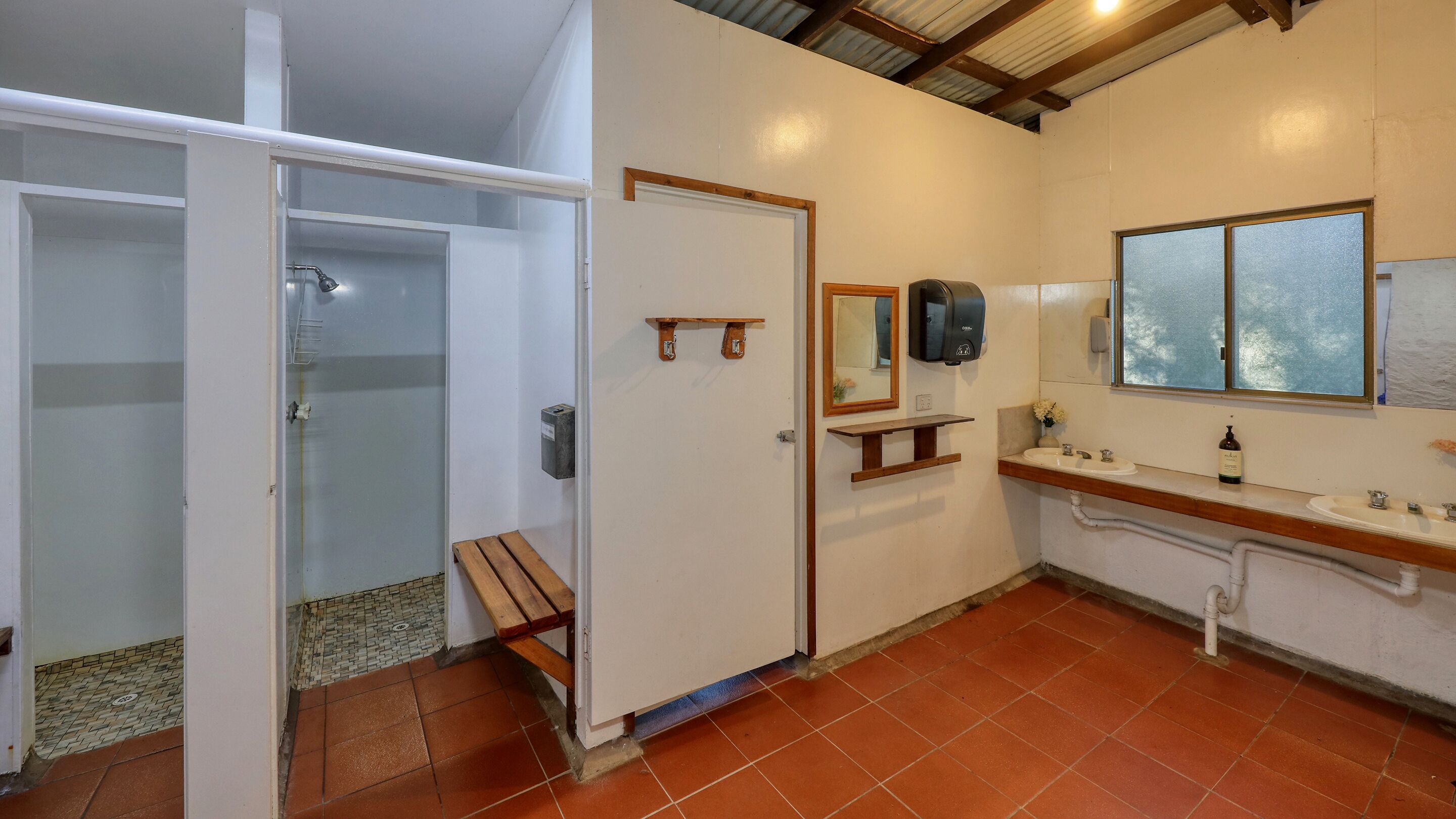 A bathroom with a shower, a bench, a sink, a mirror, and a window.