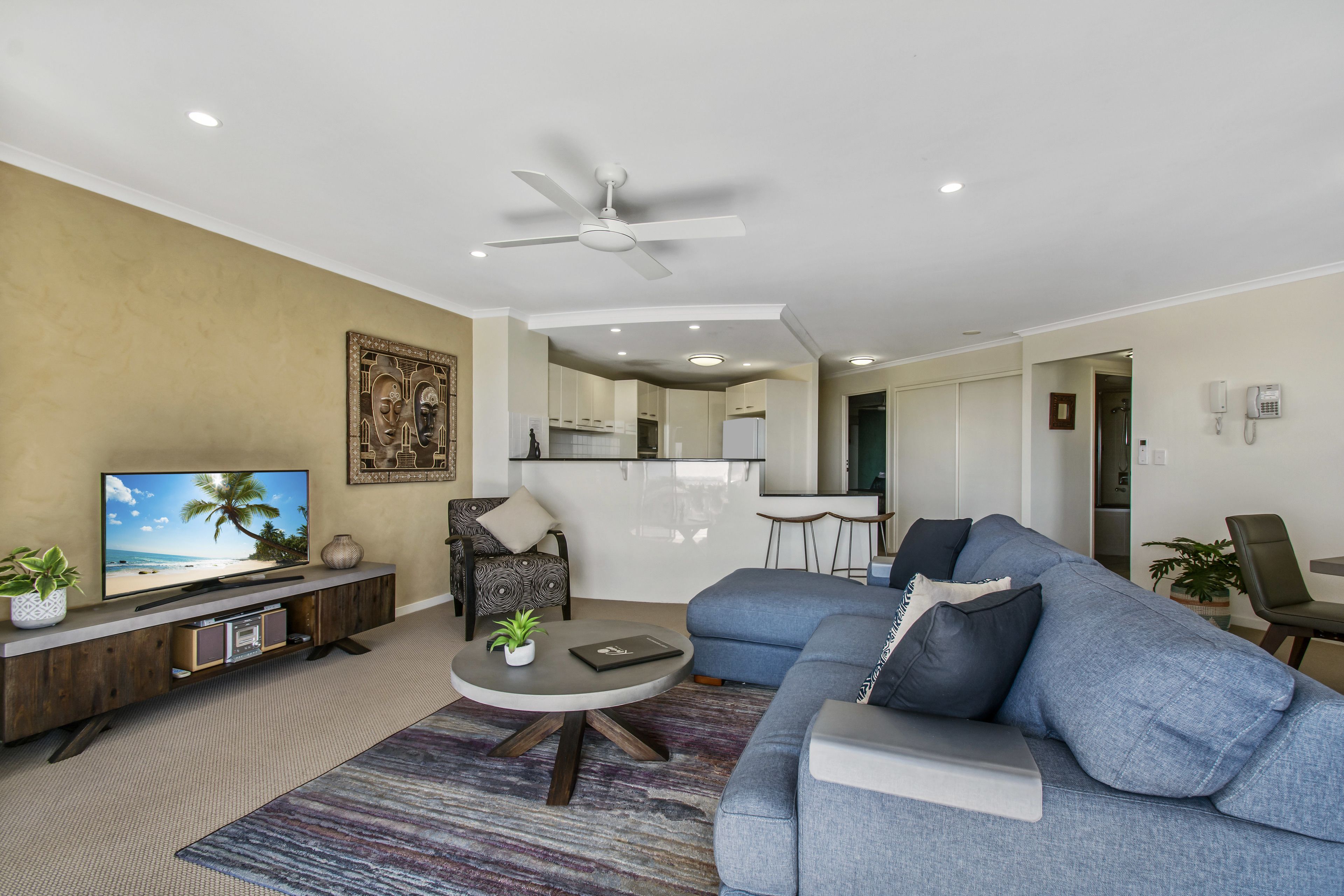 Un salon moderne avec un canapé, une table basse, un téléviseur et un ventilateur de plafond.