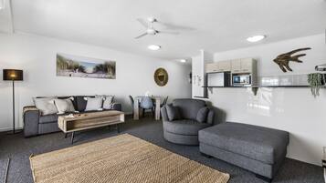 Uma sala de estar moderna com um sofá cinzento, uma poltrona cinzenta arredondada, uma mesa de centro de madeira e um tapete grande trançado.