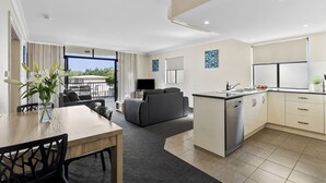 A modern kitchen with a dishwasher, a dining area with a table and chairs, a sofa, and a balcony with outdoor seating. - Cityville Apartments & Motel (Rockhampton)