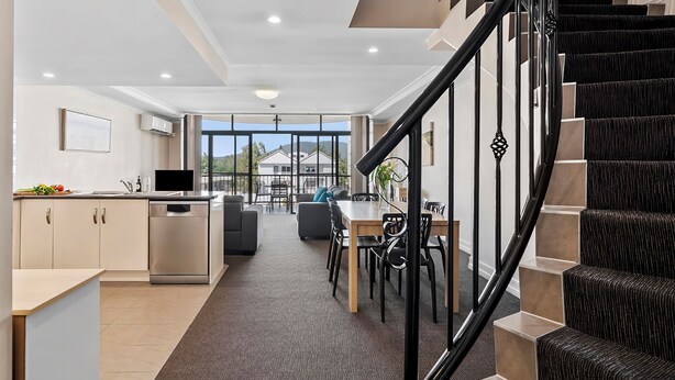 A modern kitchen with a dining area, a staircase, and a view through large windows. - Cityville Apartments & Motel (Rockhampton)