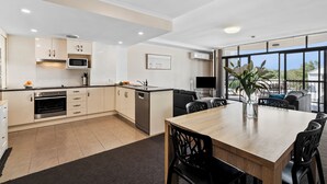 A modern kitchen with built-in appliances, a dining area with a wooden table and chairs, and large windows offering a view. - Cityville Apartments & Motel (Rockhampton)