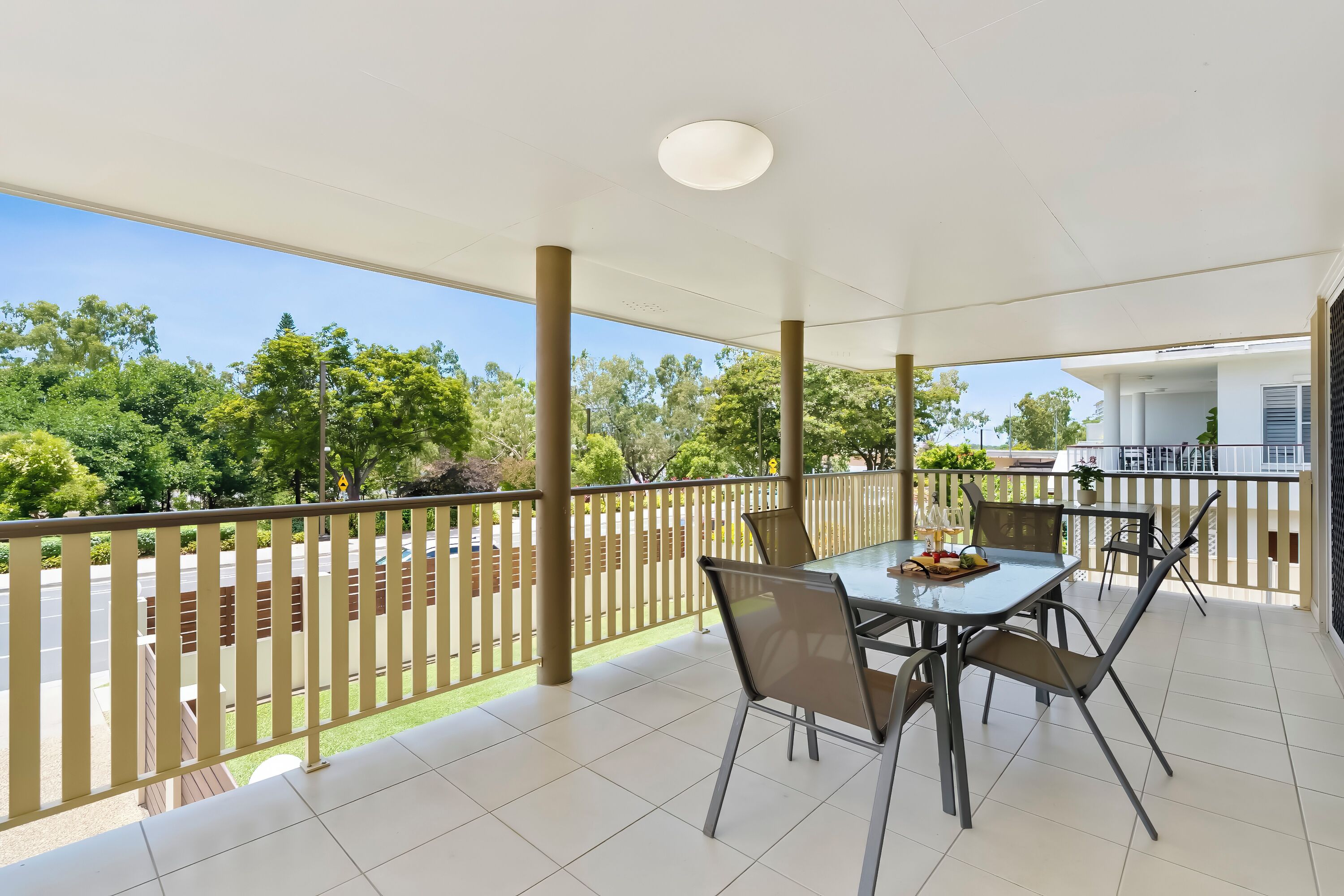 A covered outdoor area with a table and chairs, a railing, and a view of trees and a building.