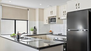 A modern kitchen with a central island, stainless steel appliances, and white cabinetry. - Cityville Apartments & Motel (Rockhampton)
