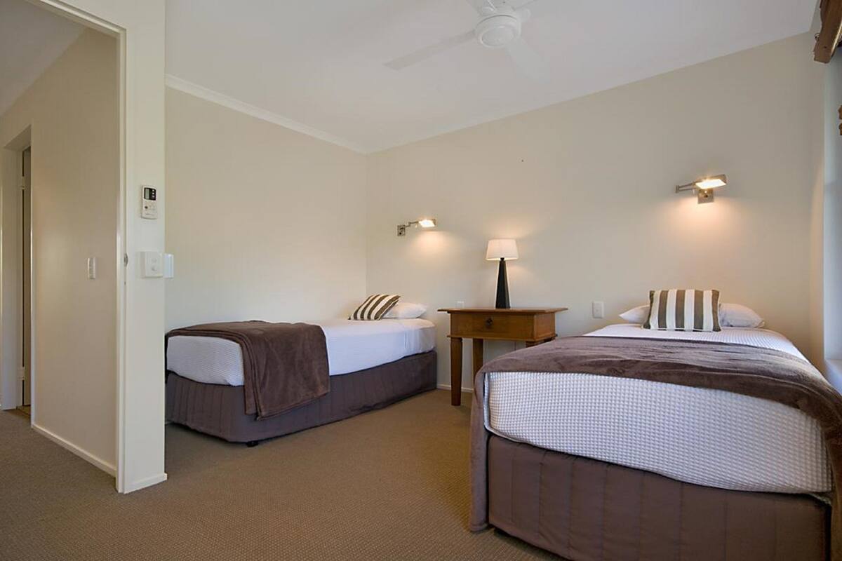 A hotel room with two beds, a nightstand, a lamp, and a ceiling fan.