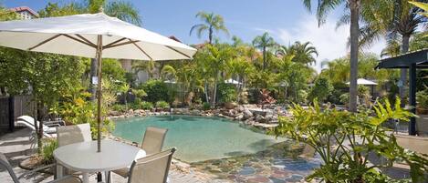A pool area with a table and chairs, surrounded by palm trees and a stone pathway.