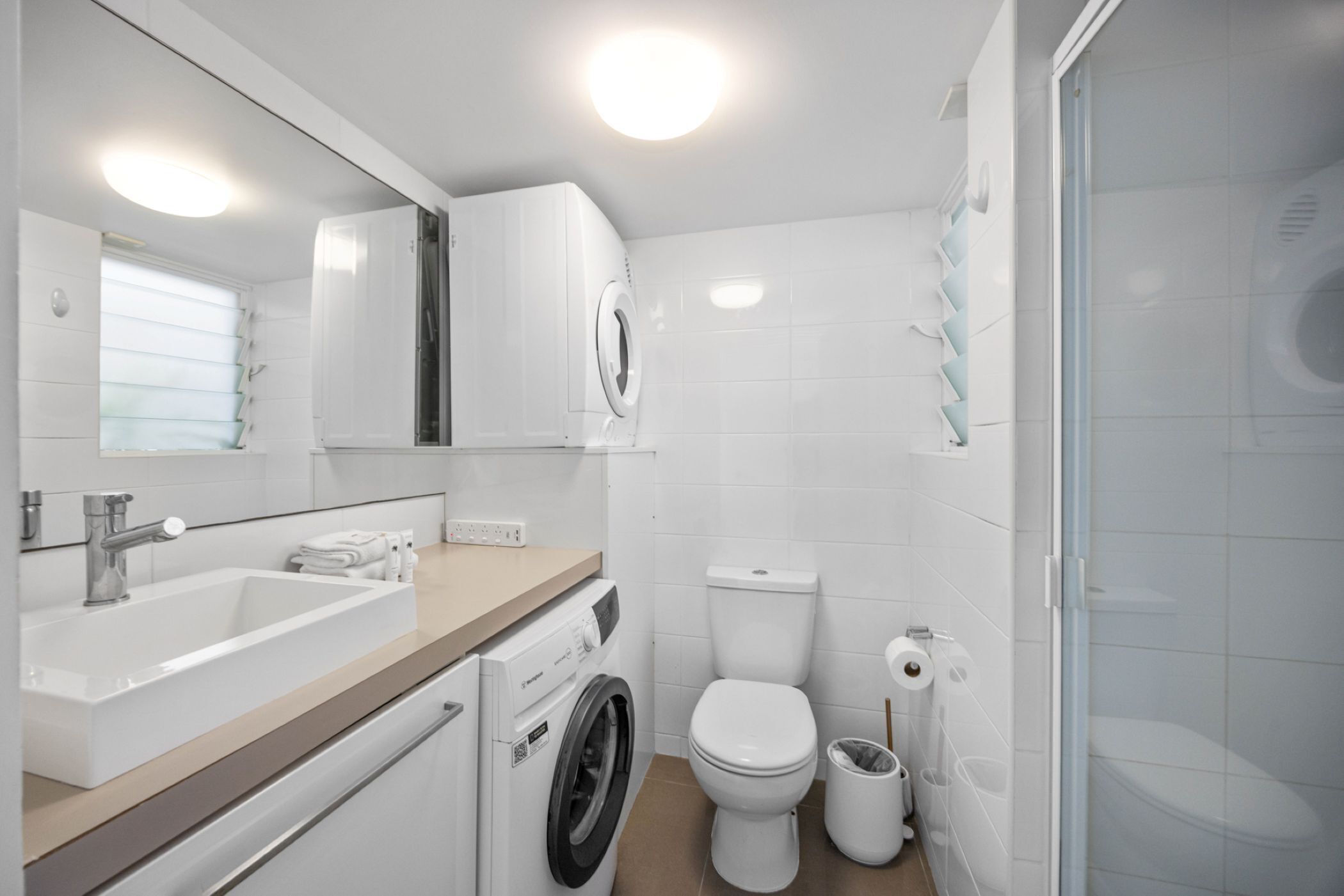 A modern bathroom with a sink, washing machine, toilet, and shower.
