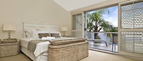 A bedroom with a bed, two nightstands, a ceiling fan, and a balcony with a view of palm trees.
