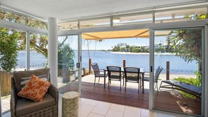 A sunlit room with a view of the sea, a wooden deck, and a glass door leading outside. - Skippers Cove Waterfront Resort (Noosaville)