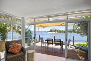 A sunlit room with a view of the sea, a wooden deck, and a glass door leading outside.