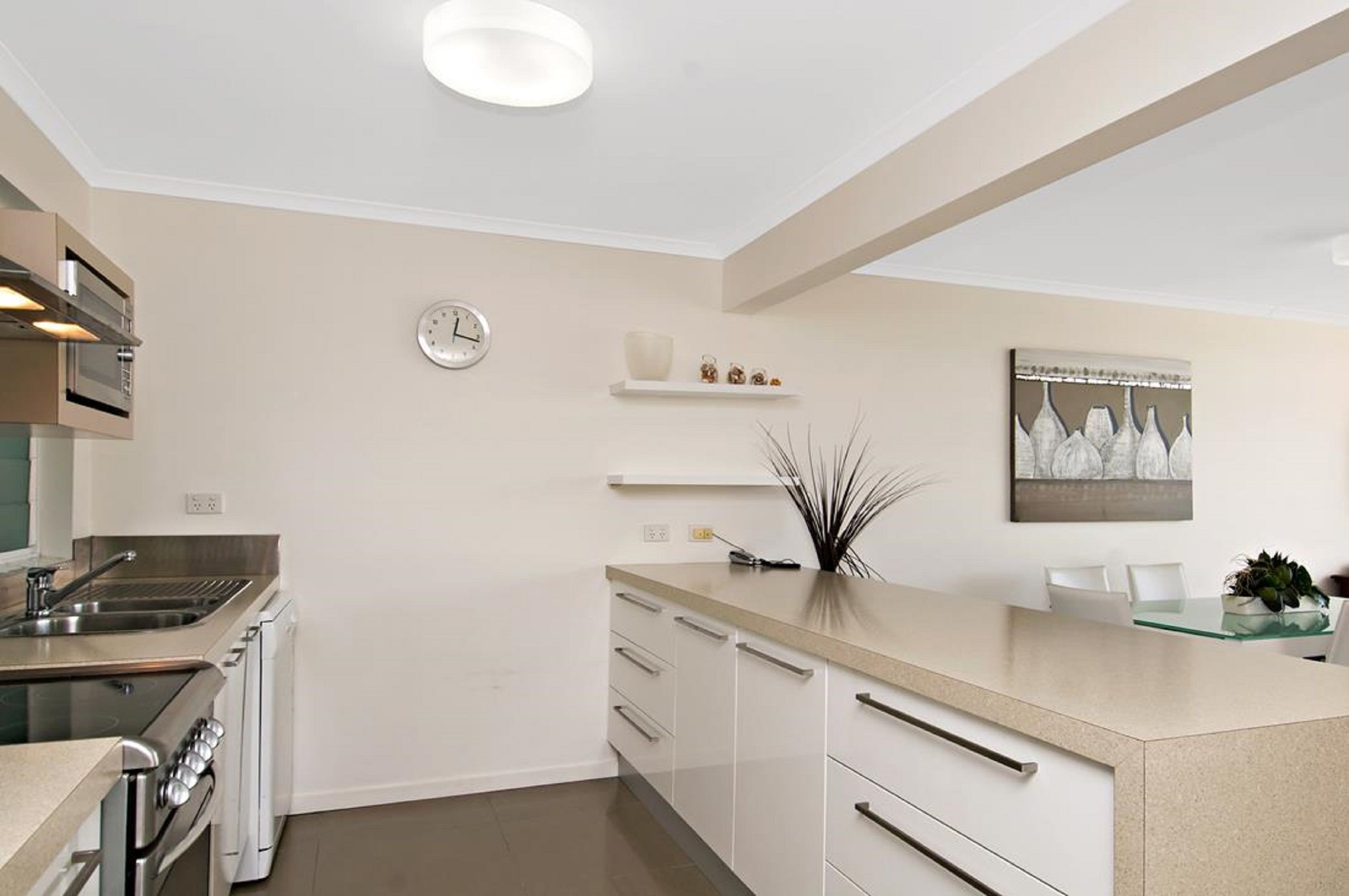 A modern kitchen with a built-in oven, a sink, and a dining area with a glass table and chairs.