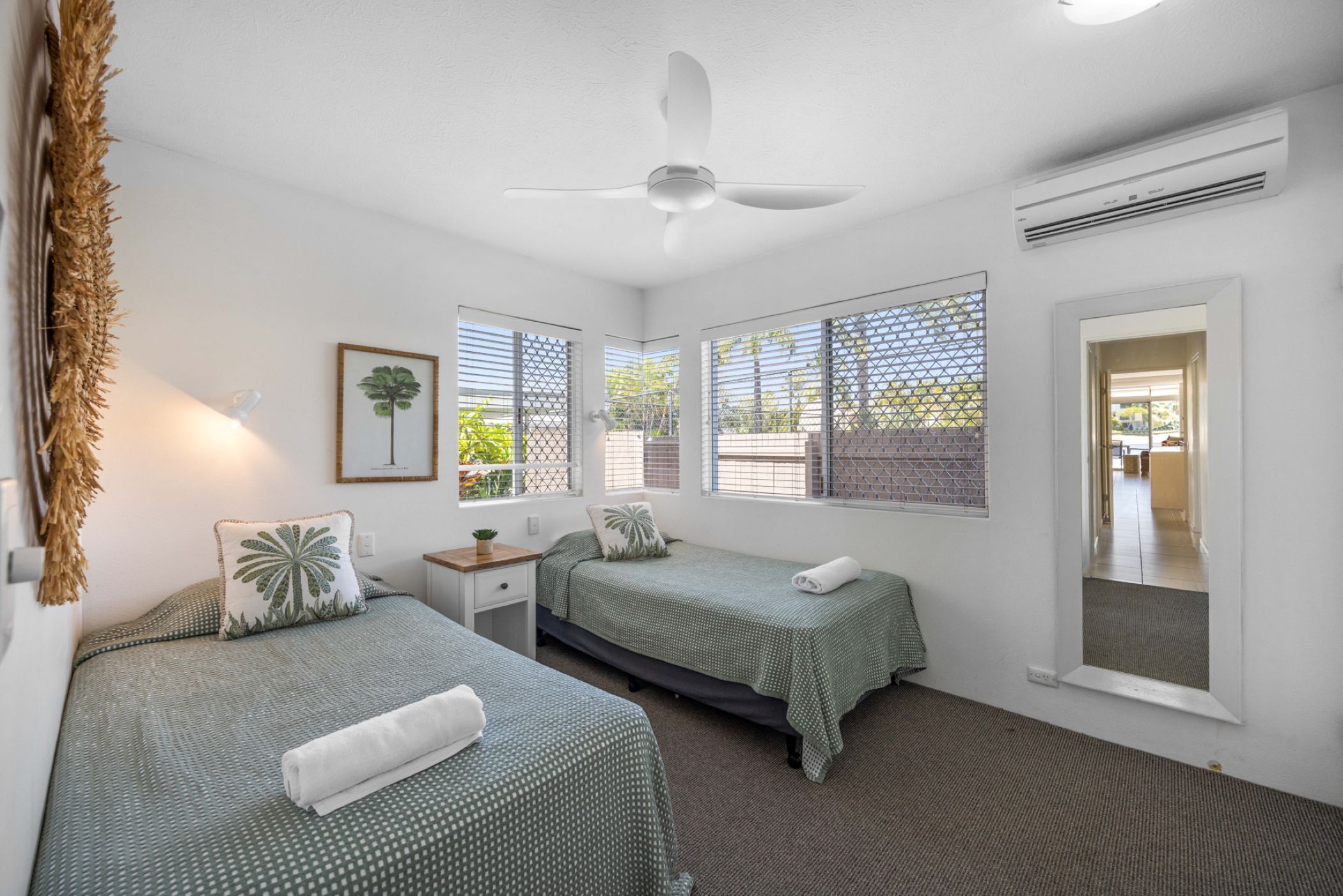 Une chambre avec deux lits, un ventilateur de plafond, un appareil de climatisation et une fenêtre donnant sur un paysage verdoyant.