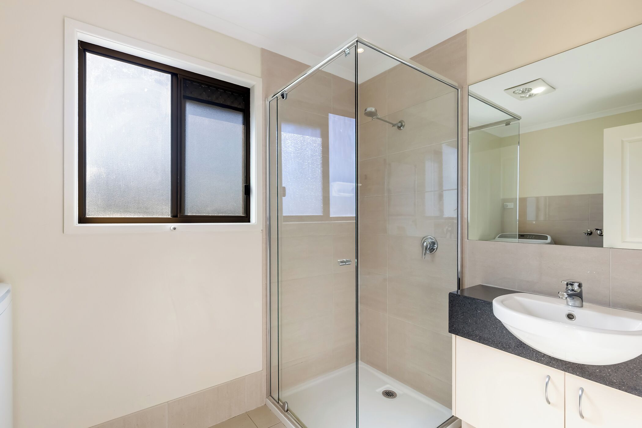 Une salle de bain avec une douche à parois de verre, un lavabo et une fenêtre.