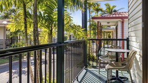 A balcony with a table and chairs, surrounded by palm trees and a red-roofed structure. - Brisbane Gateway Resort (Rochedale)