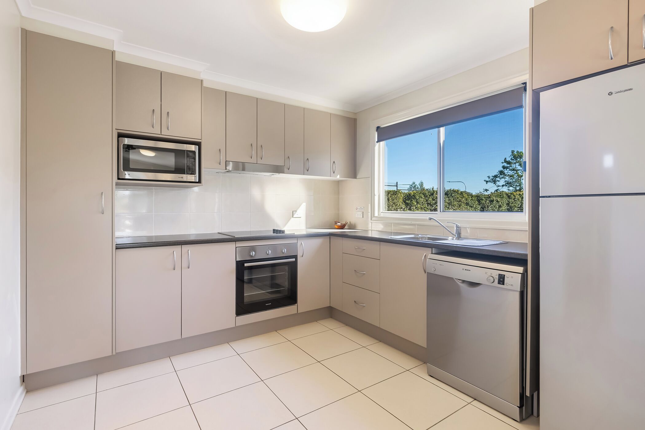 A modern kitchen with a built-in oven, microwave, dishwasher, and a window with a view.