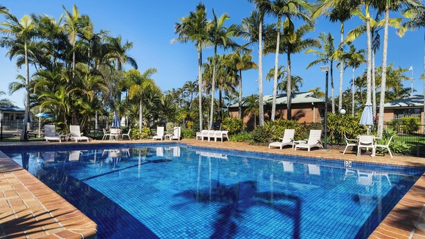 A clear blue pool surrounded by palm trees and white lounge chairs. - Brisbane Gateway Resort (Rochedale)