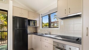 A modern kitchen with a black refrigerator, stainless steel appliances, and a window with a view of palm trees. - Brisbane Gateway Resort (Rochedale)
