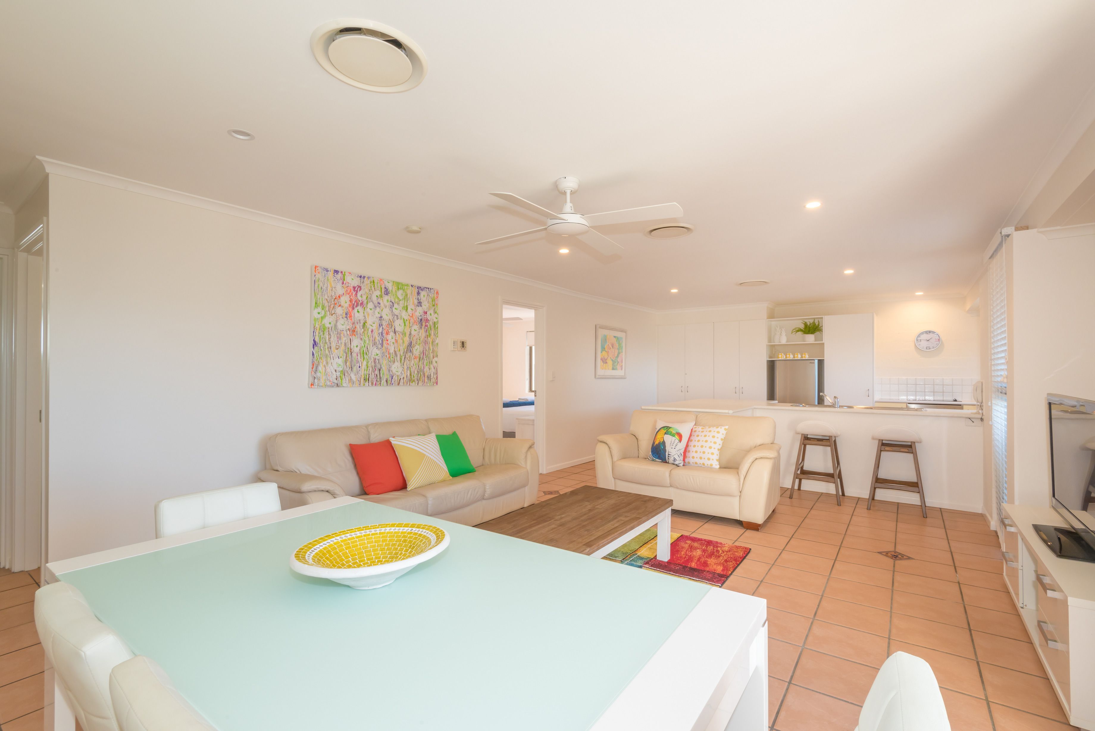 Amplia sala de estar con una mesa de comedor, dos sofás, una zona de cocina y un ventilador de techo.
