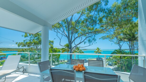 A balcony with a glass table, chairs, and a bowl of oranges. - Munna Beach Apartments (Noosaville)