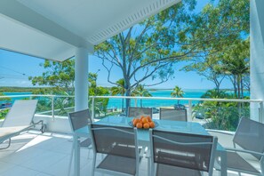 A balcony with a glass table, chairs, and a bowl of oranges. - Munna Beach Apartments (Noosaville)