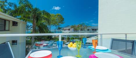A balcony table set with colorful plates and glasses, overlooking a pool and palm trees.