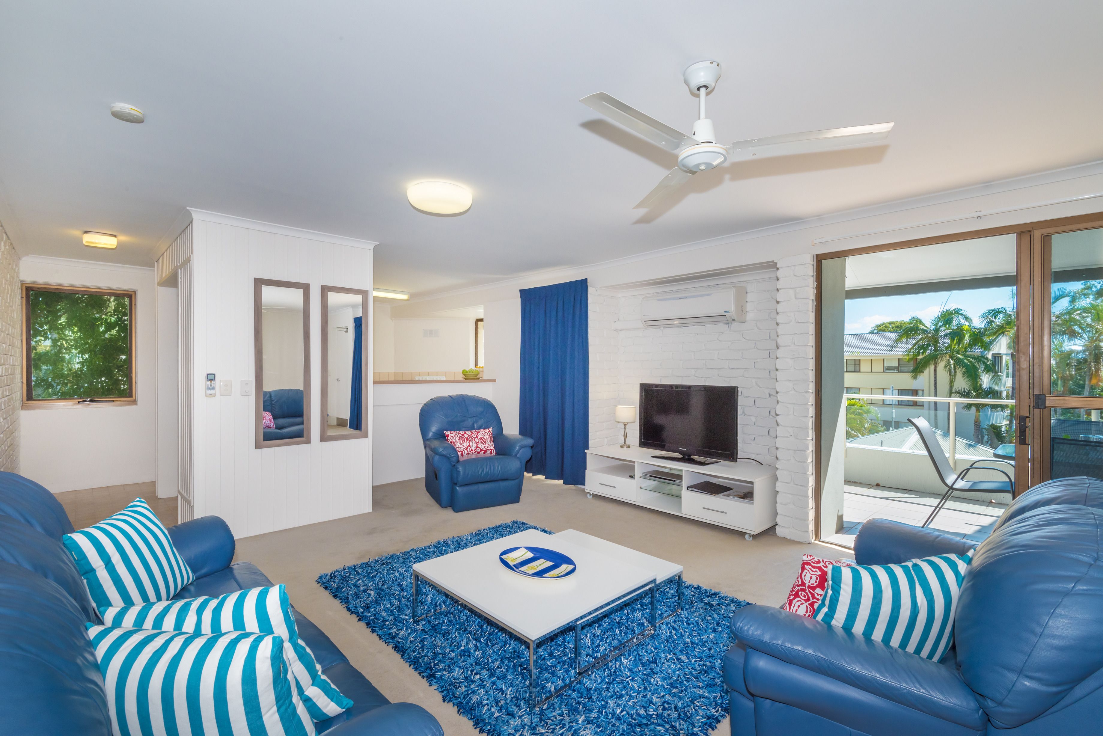 A modern living room with a white brick fireplace, a flat-screen TV, and a ceiling fan.