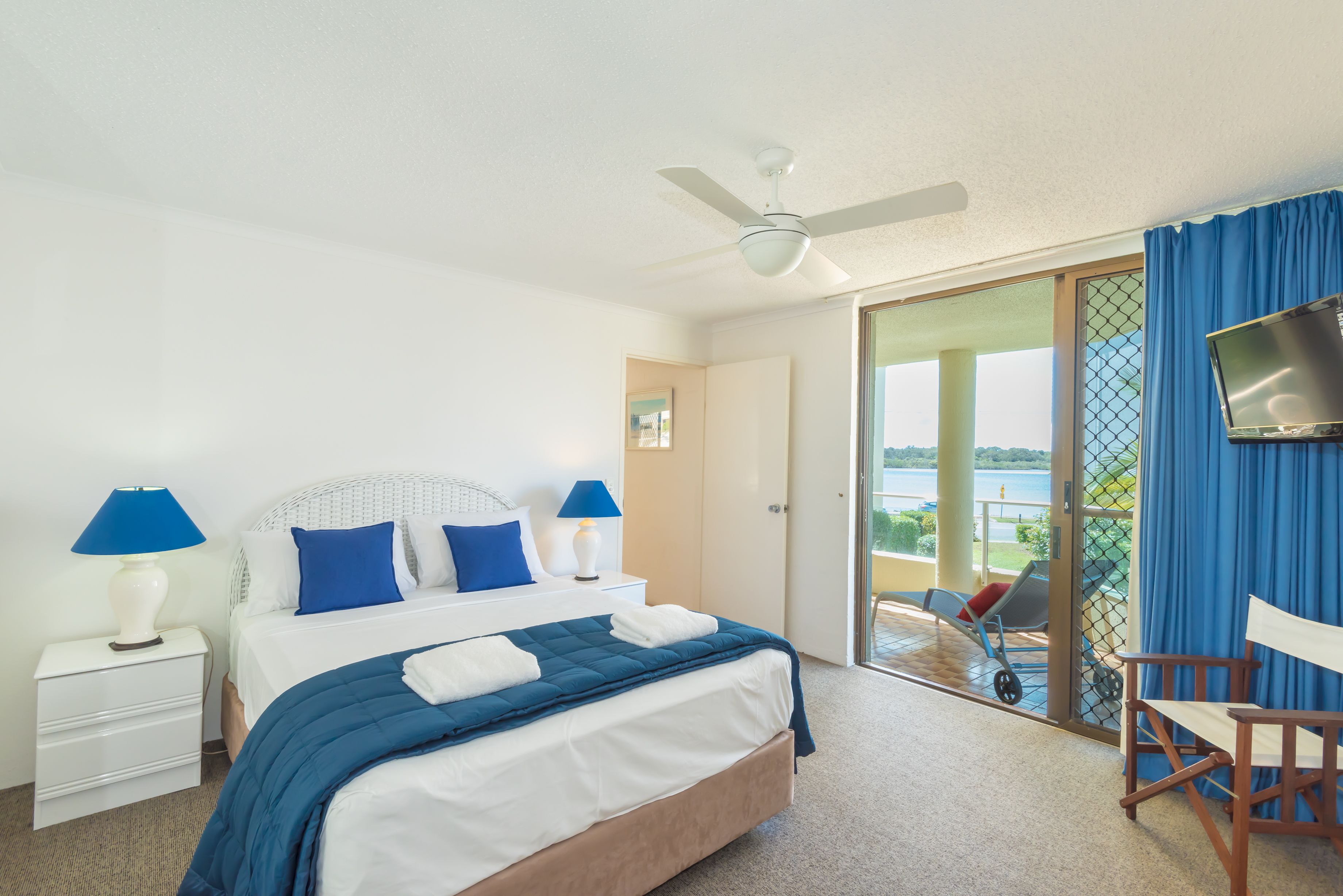 A hotel room with a bed, a TV, a chair, and a balcony with a view.