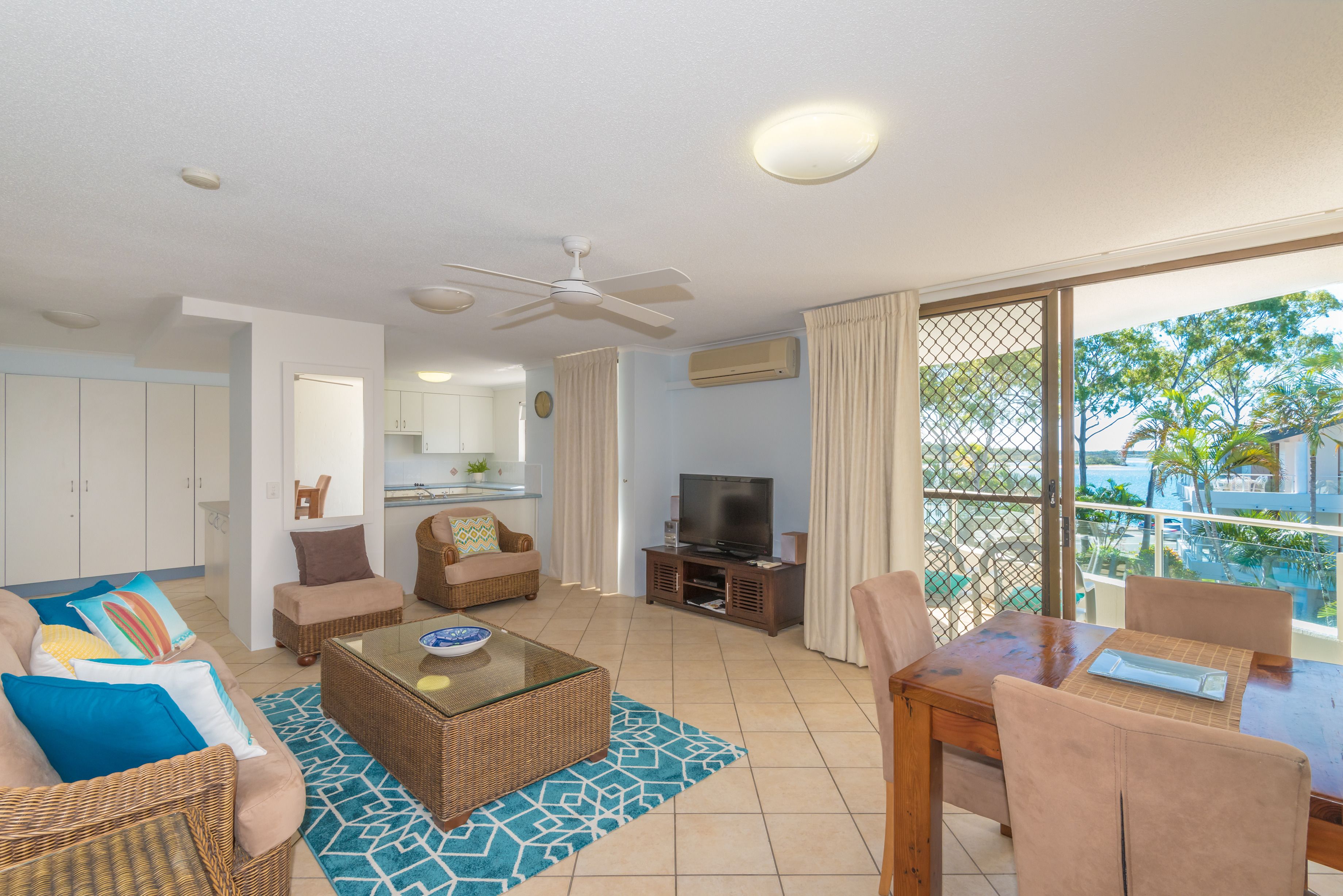 Uma sala de estar espaçosa com televisão, móveis de vime e uma varanda com vista para a piscina.