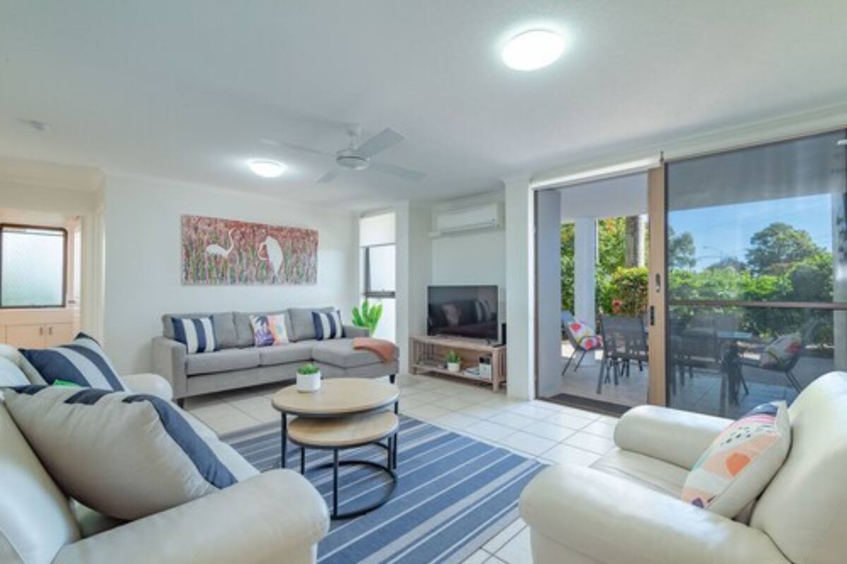 A modern living room with a sofa, armchairs, a coffee table, a TV, and a balcony with outdoor furniture.