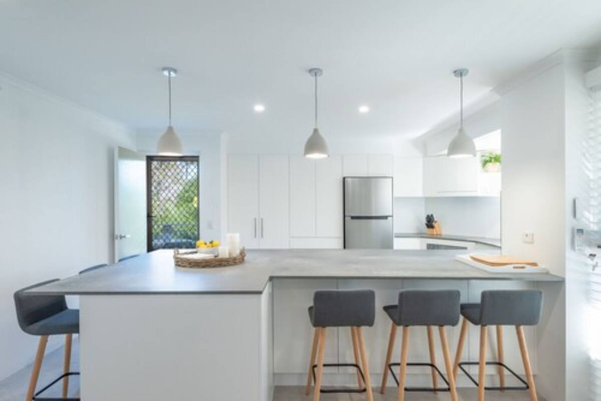 A modern kitchen with a central island, bar stools, pendant lighting, and a refrigerator.