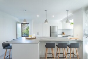 Una cocina moderna con una isla central, taburetes de bar, iluminación colgante y un refrigerador.