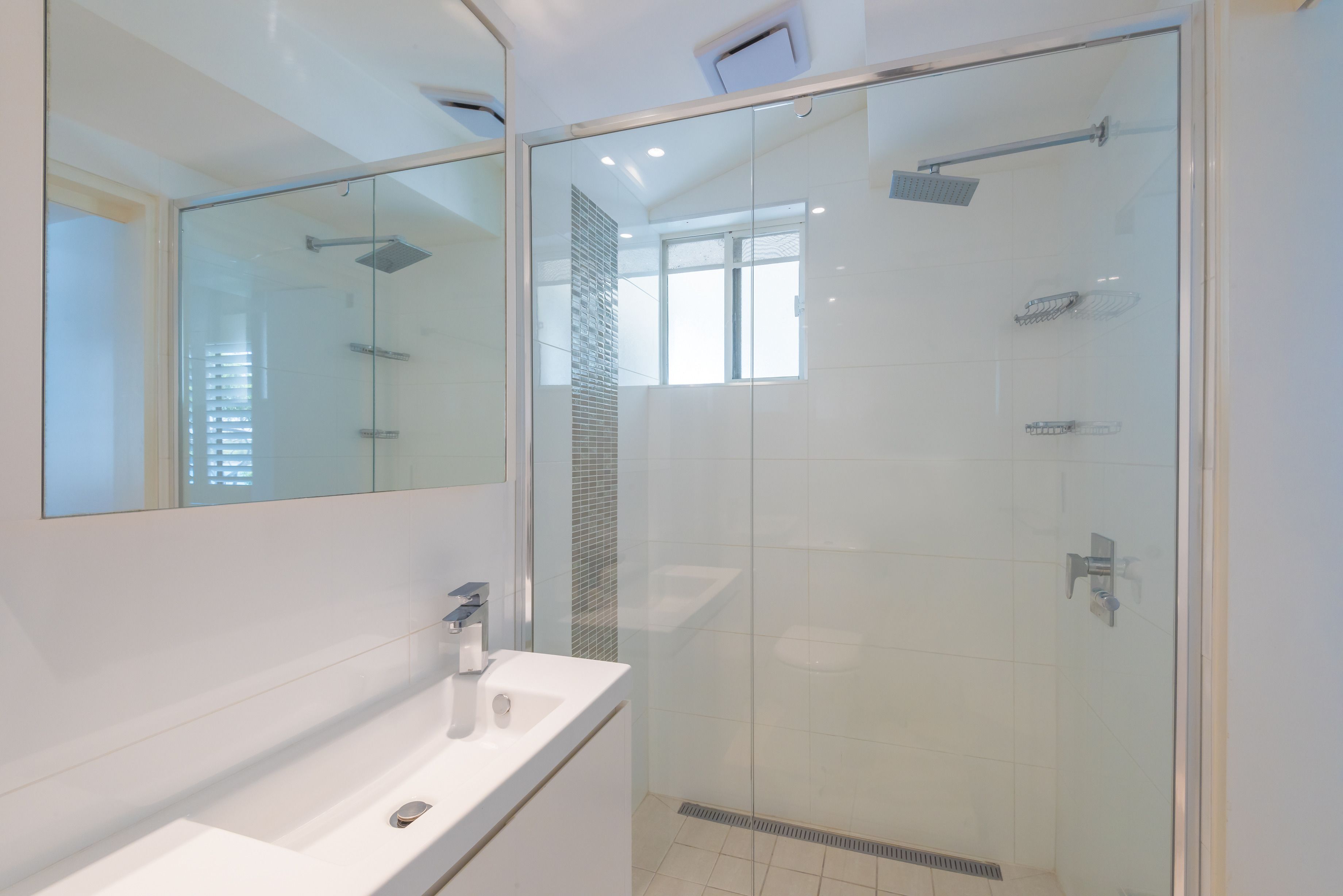 A modern bathroom with a glass-enclosed shower, a large mirror, and a white sink.