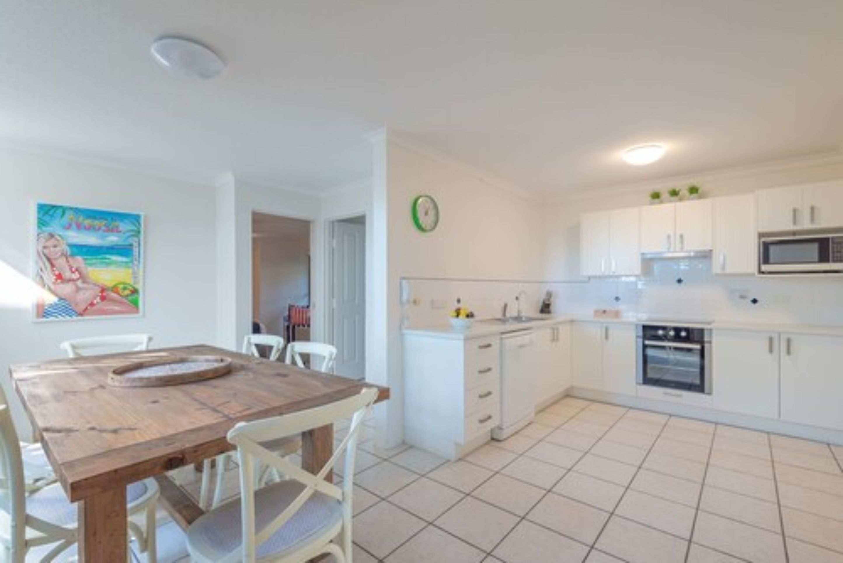 Una cocina moderna con armarios blancos, microondas y horno. Hay una mesa de comedor con sillas y un cuadro en la pared.