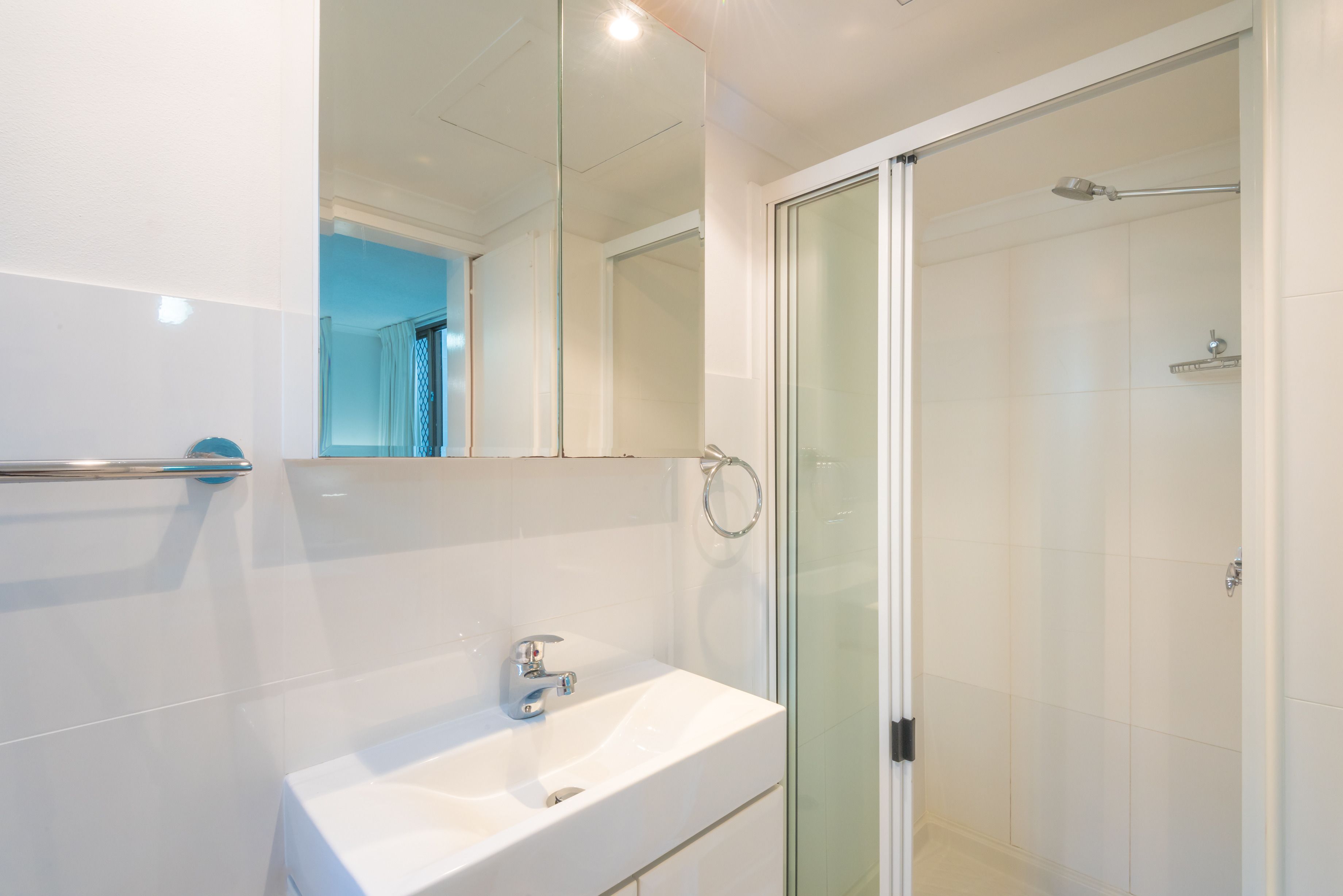 A modern bathroom with a white sink, a glass shower enclosure, and a large mirror.