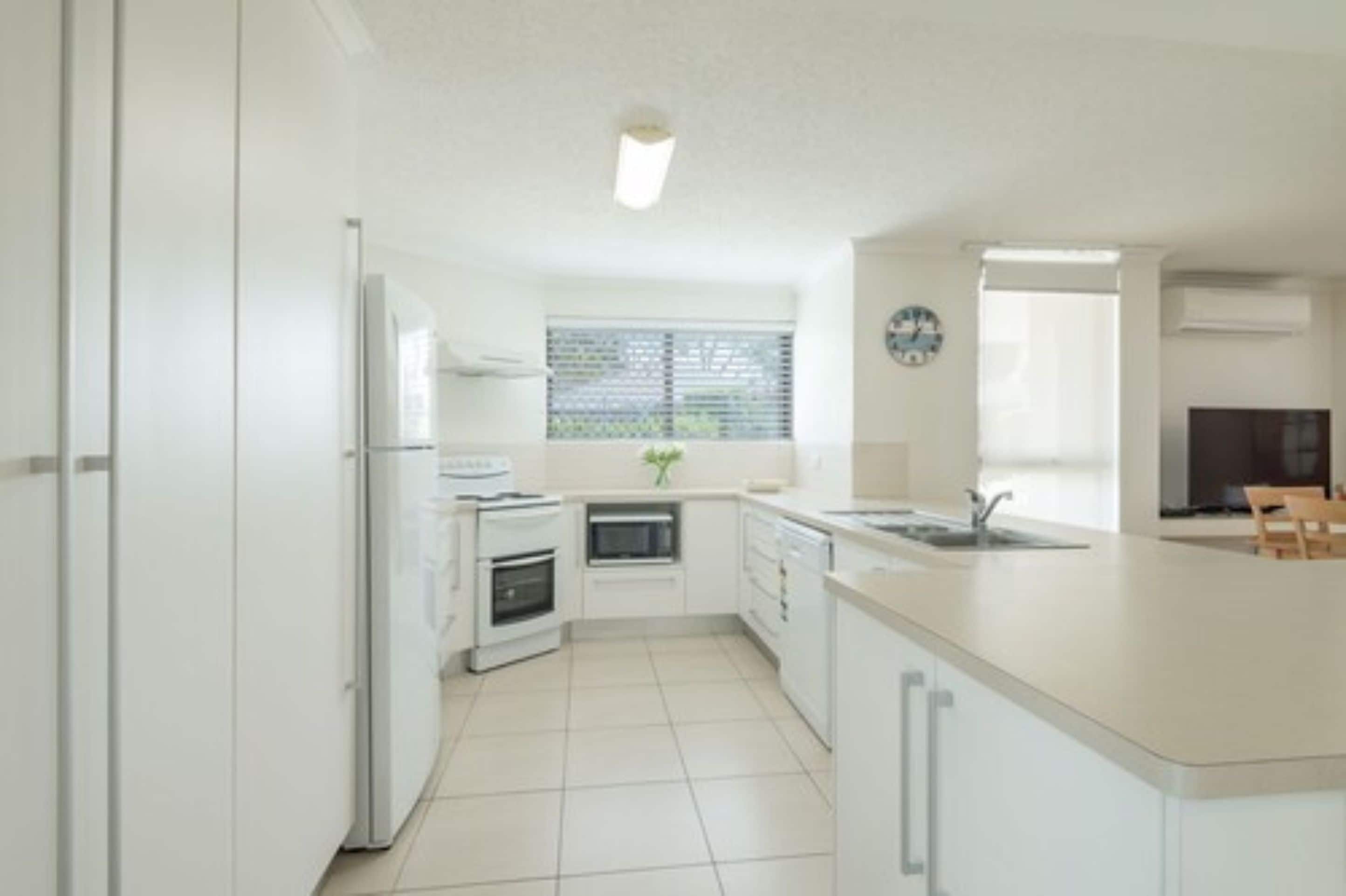 A modern kitchen with white cabinets, a built-in oven, a microwave, and a large island with a sink.