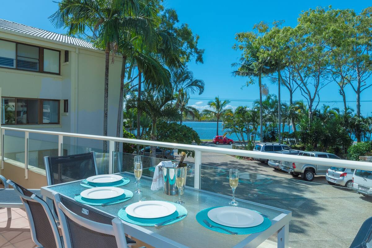 A dining table set for four with a view of the ocean and palm trees.