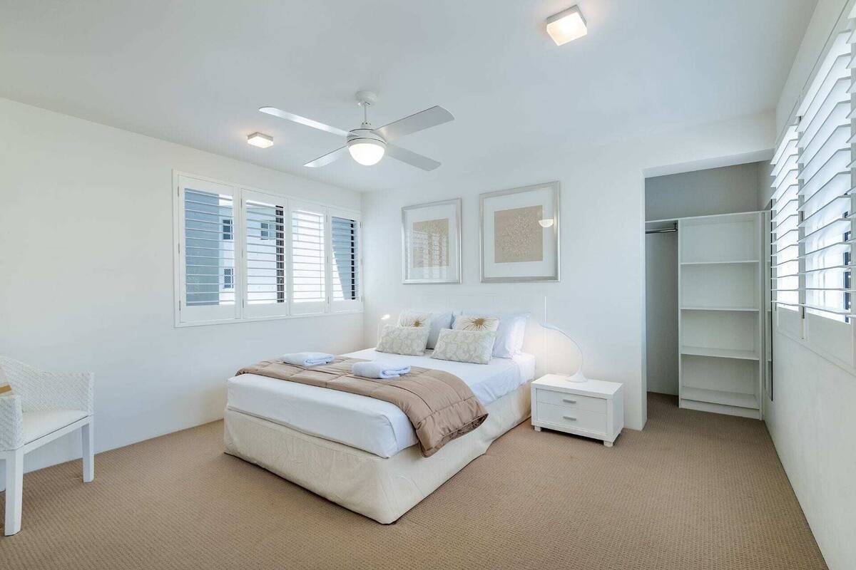 A bedroom with a bed, bedside tables, a ceiling fan, and a walk-in closet.