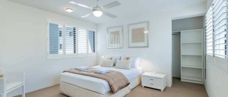 Un dormitorio con cama, mesitas de noche, ventilador de techo y vestidor.