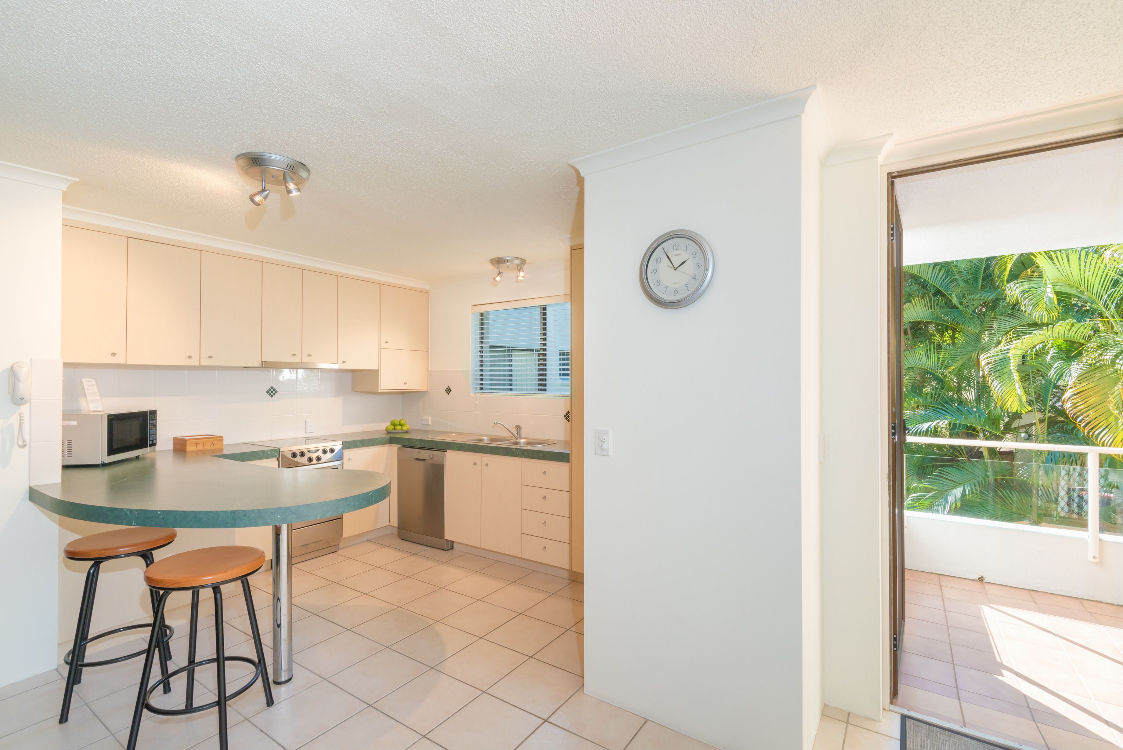 A kitchen with a central island, two stools, a microwave, a stove, and a dishwasher.