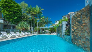 A swimming pool with lounge chairs and a stone wall. - Munna Beach Apartments (Noosaville)