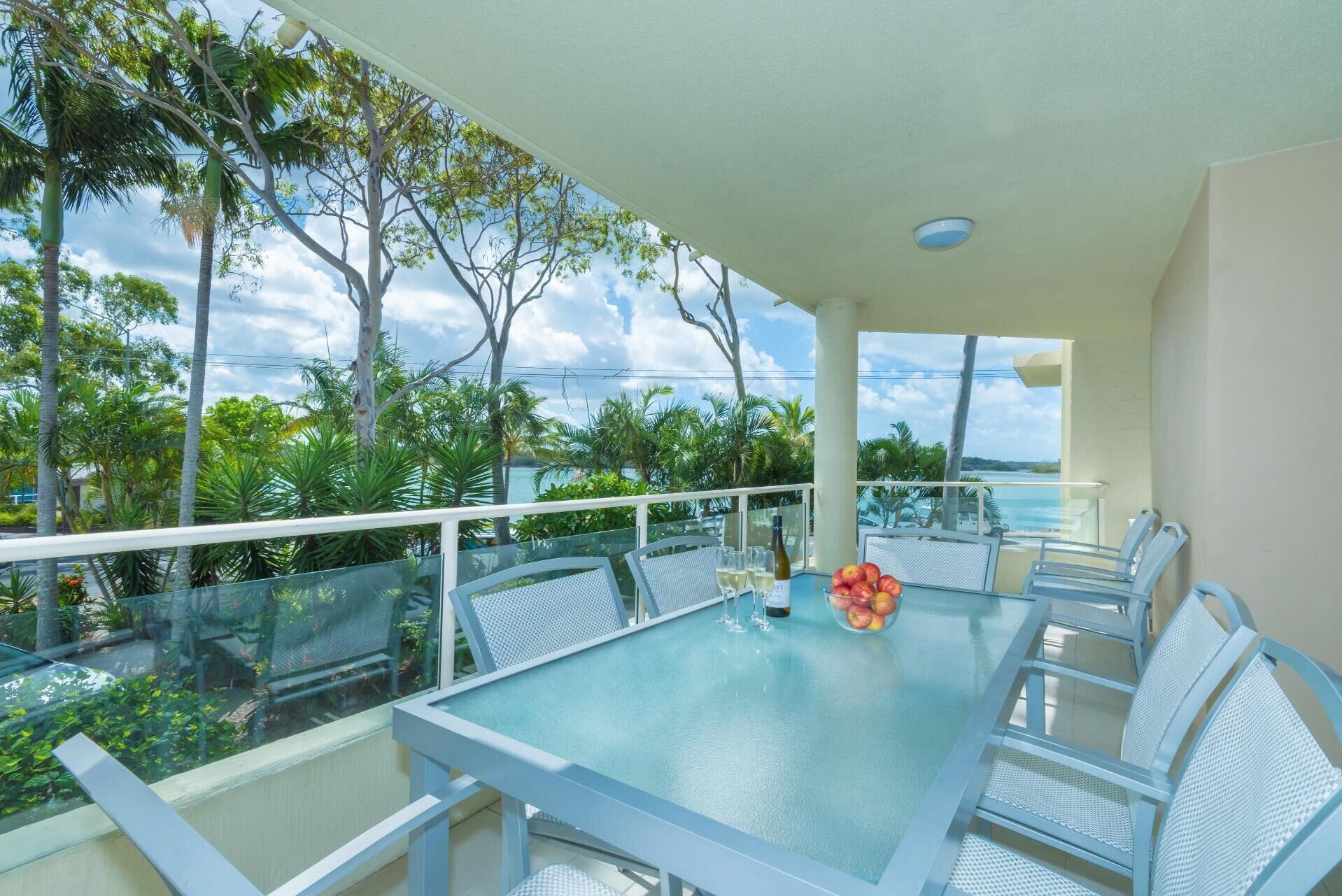 A balcony with a glass table, white chairs, and a bottle of wine.