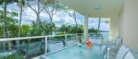 A balcony with a glass table, white chairs, and a bottle of wine.