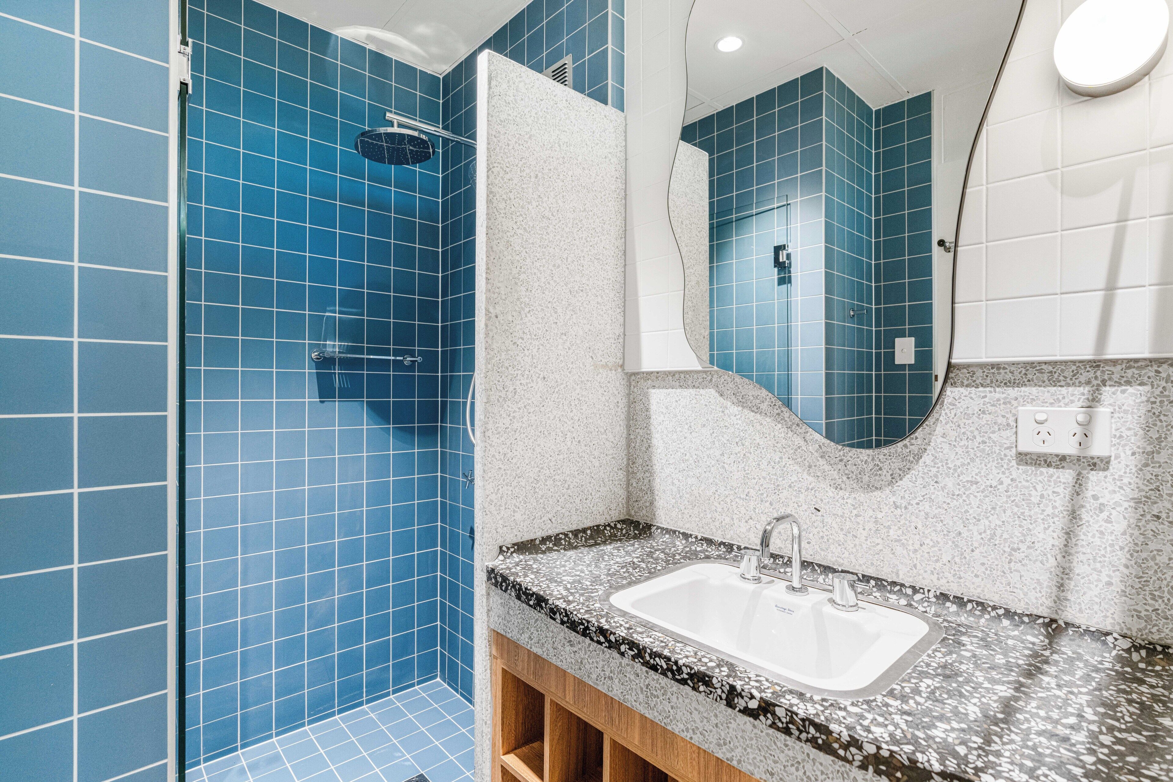A bathroom with blue tiles, a white sink, and a mirror.
