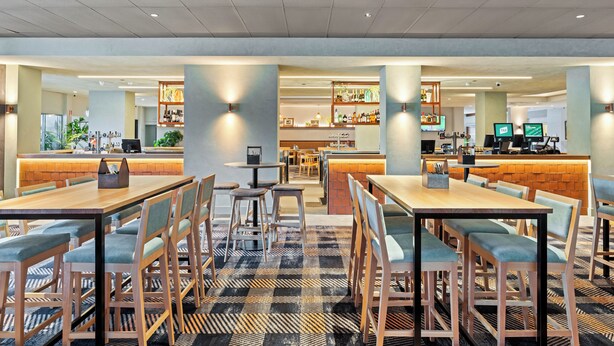 Un restaurante moderno con varias zonas de estar, incluyendo mesas y cabinas, y una barra al fondo.